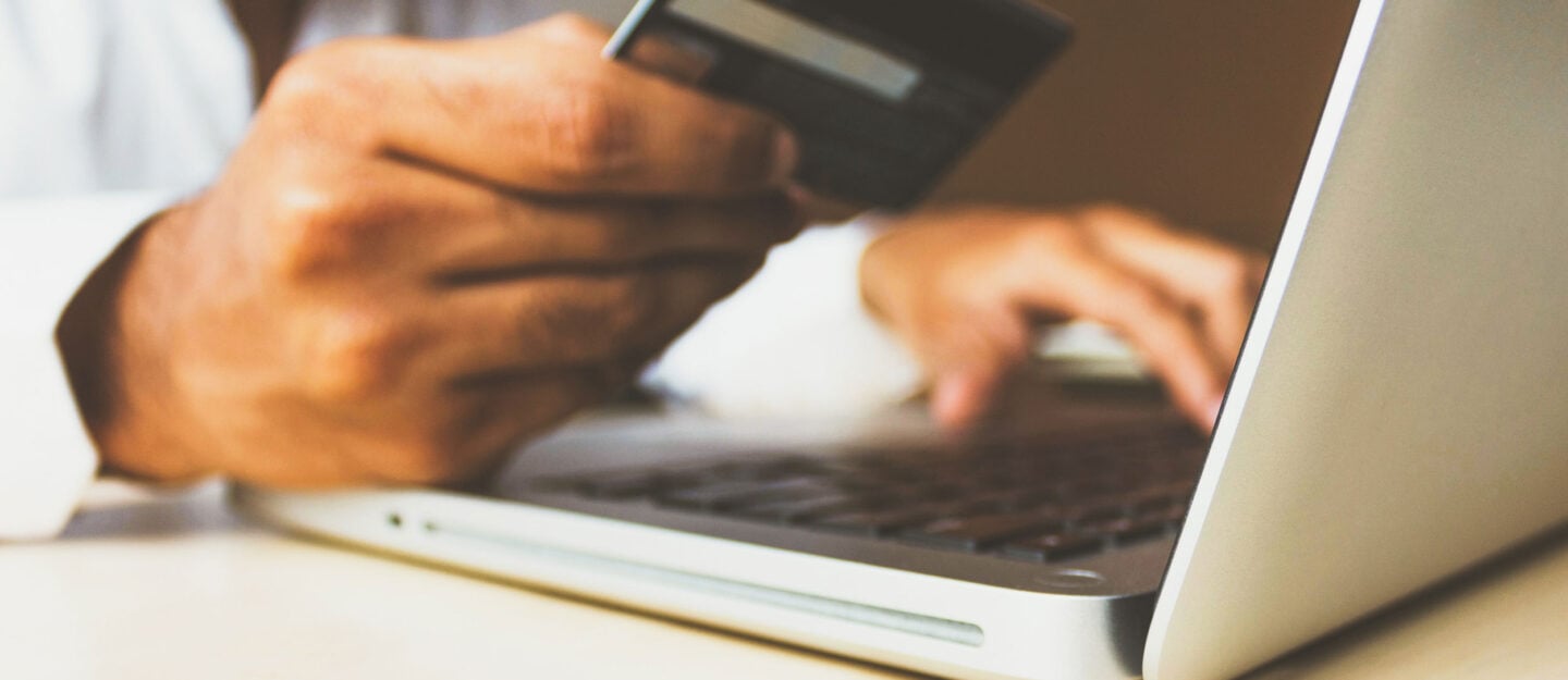 man holds creditcard in his hand sitting in front of a laptop